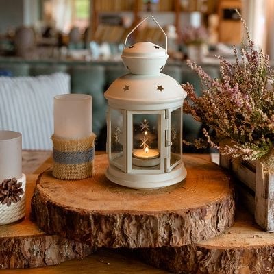 Picture of a lantern on a rustic wood table flanked by flowers and candle